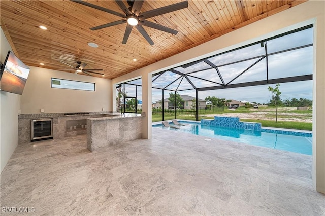 view of pool featuring exterior bar, an outdoor kitchen, glass enclosure, and a patio area