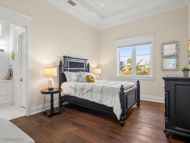 bedroom with connected bathroom, dark wood-type flooring, ornamental molding, and a raised ceiling