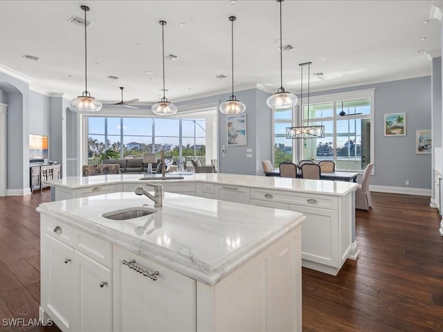 kitchen with sink, hanging light fixtures, an island with sink, light stone countertops, and white cabinets