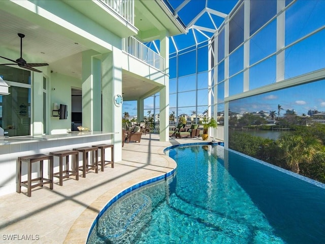 view of swimming pool featuring a bar, ceiling fan, a water view, and a patio area