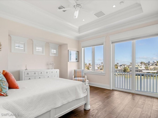 bedroom featuring crown molding, a water view, wood-type flooring, a raised ceiling, and access to exterior