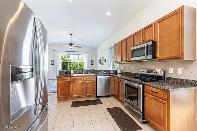 kitchen featuring lofted ceiling, ceiling fan, dark stone countertops, kitchen peninsula, and appliances with stainless steel finishes