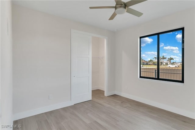 unfurnished bedroom featuring a walk in closet, light wood-type flooring, a closet, and ceiling fan