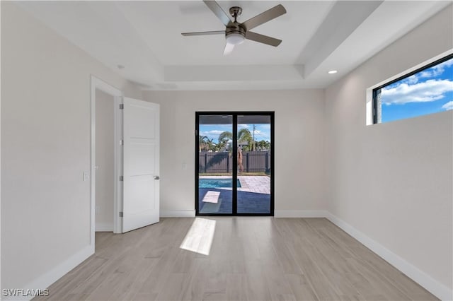 empty room with a raised ceiling, ceiling fan, and light hardwood / wood-style floors