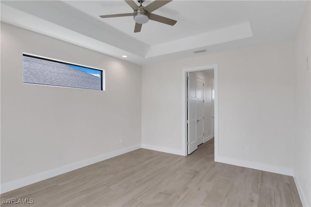 empty room with light hardwood / wood-style flooring, a raised ceiling, and ceiling fan