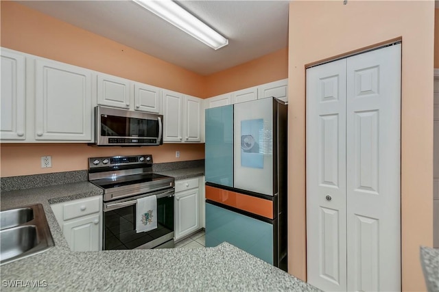 kitchen featuring stainless steel appliances, light tile patterned flooring, white cabinetry, and sink