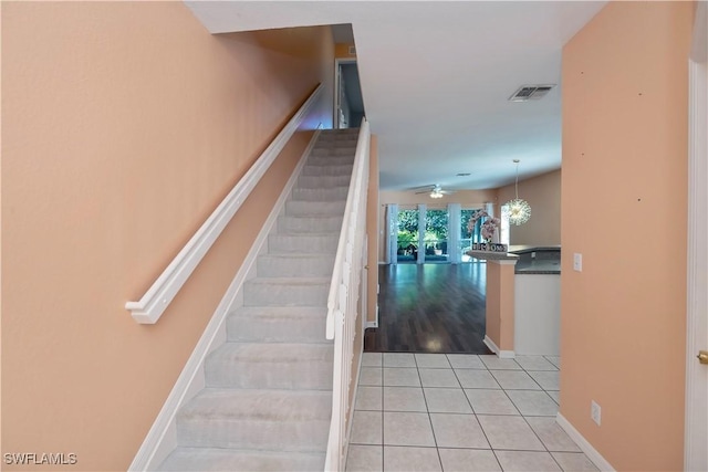 stairway featuring ceiling fan with notable chandelier and tile patterned flooring