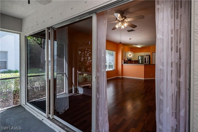 doorway to outside featuring ceiling fan with notable chandelier and dark wood-type flooring