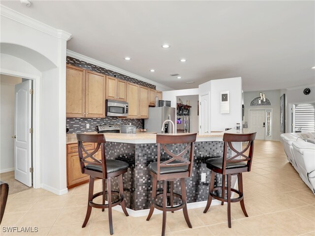 kitchen featuring a breakfast bar, backsplash, appliances with stainless steel finishes, light countertops, and light tile patterned floors