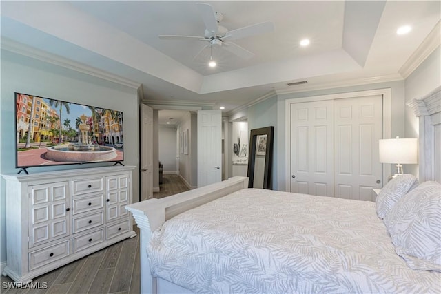 bedroom with ceiling fan, a raised ceiling, dark hardwood / wood-style flooring, a closet, and ornamental molding