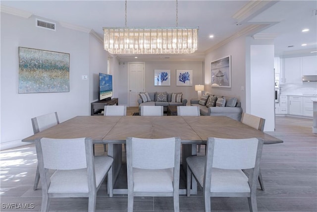 dining space featuring a chandelier, light wood-type flooring, and crown molding