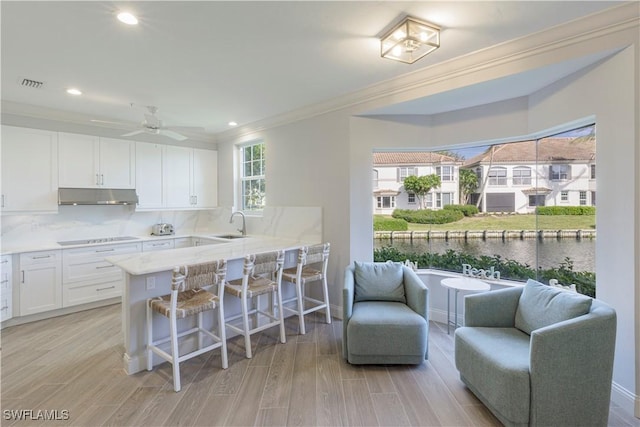 kitchen with kitchen peninsula, cooktop, light hardwood / wood-style floors, white cabinetry, and a breakfast bar area