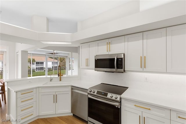 kitchen featuring white cabinetry, sink, kitchen peninsula, stainless steel appliances, and light hardwood / wood-style flooring