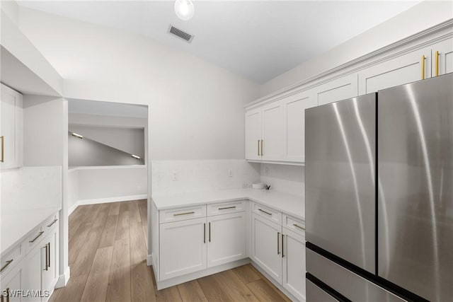 kitchen with white cabinetry, light stone counters, stainless steel refrigerator, and light hardwood / wood-style flooring