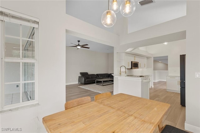 dining room with sink, ceiling fan with notable chandelier, and light wood-type flooring