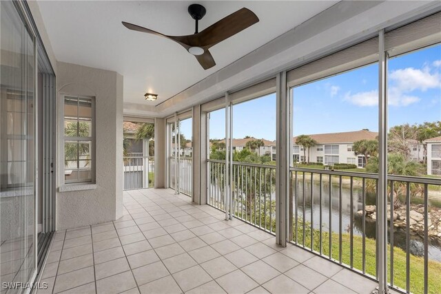 unfurnished sunroom featuring ceiling fan and a water view