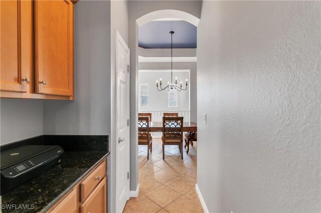 kitchen with light tile patterned floors, pendant lighting, an inviting chandelier, and dark stone counters