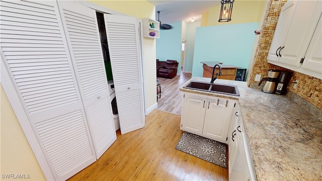 kitchen featuring light wood-type flooring, decorative light fixtures, white cabinetry, and sink