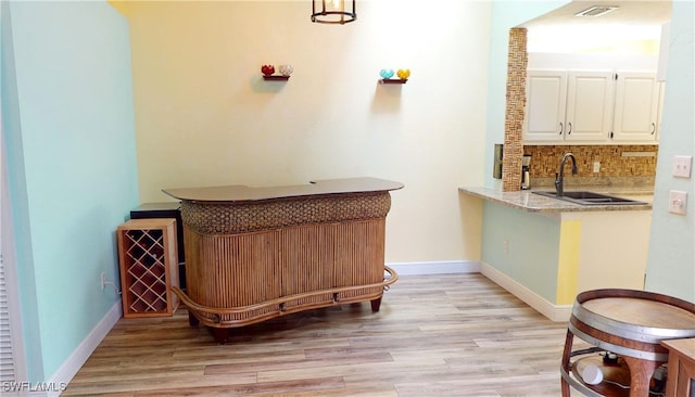 bar featuring decorative backsplash, light hardwood / wood-style floors, white cabinetry, and sink