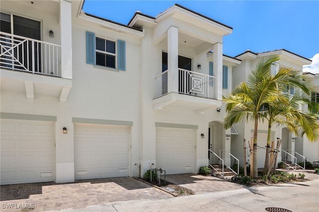 multi unit property with driveway, a balcony, a garage, and stucco siding