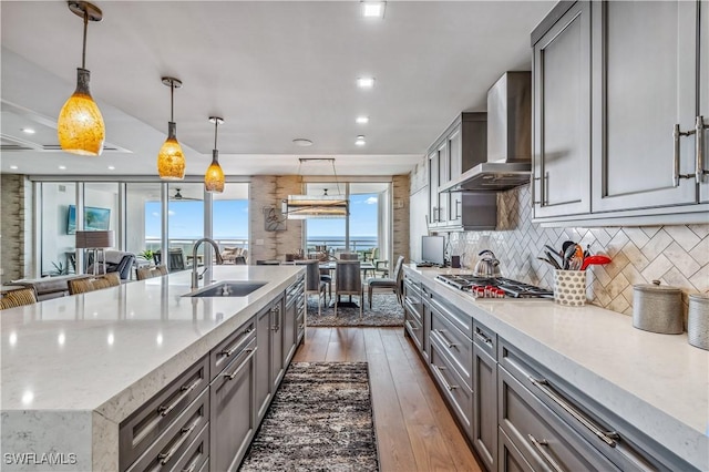 kitchen featuring sink, wall chimney exhaust hood, stainless steel gas cooktop, a large island with sink, and pendant lighting