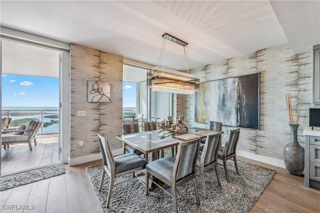 dining space with expansive windows, light hardwood / wood-style floors, and a water view