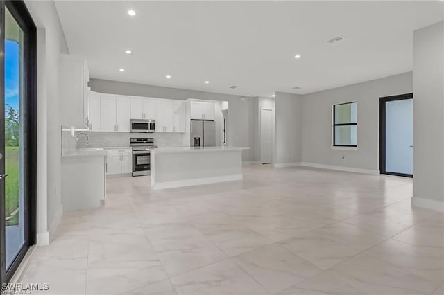 kitchen with sink, stainless steel appliances, a kitchen island, tasteful backsplash, and white cabinets