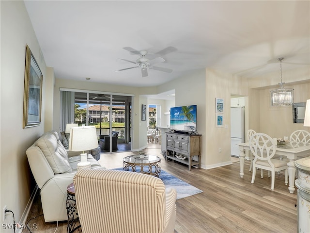 living room with ceiling fan with notable chandelier and light wood-type flooring