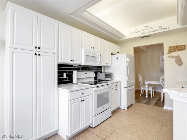 kitchen with white appliances, a raised ceiling, light tile patterned floors, tasteful backsplash, and white cabinetry