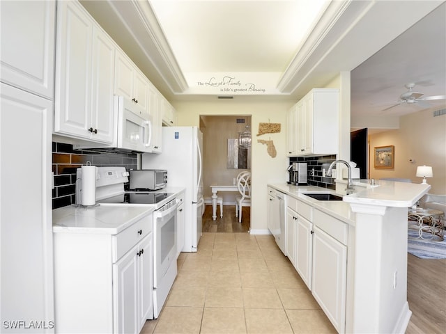 kitchen featuring white appliances, kitchen peninsula, a raised ceiling, and white cabinets