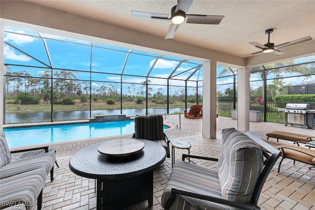 view of patio featuring grilling area, ceiling fan, glass enclosure, and a water view