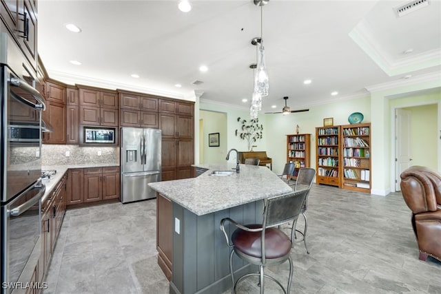 kitchen with light stone countertops, appliances with stainless steel finishes, hanging light fixtures, ceiling fan, and a center island with sink