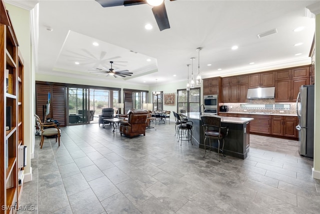 kitchen with a kitchen bar, appliances with stainless steel finishes, a raised ceiling, a spacious island, and pendant lighting