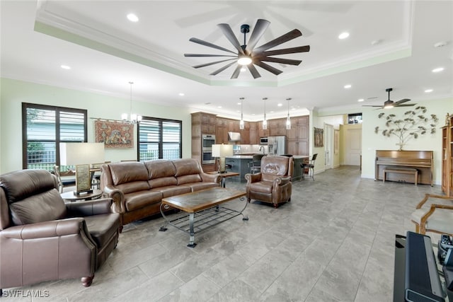 living room with ceiling fan with notable chandelier, a tray ceiling, and ornamental molding