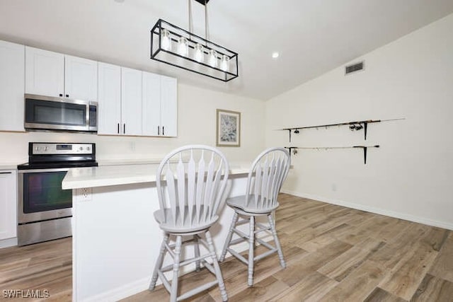 kitchen with white cabinets, light wood-type flooring, decorative light fixtures, stainless steel appliances, and vaulted ceiling