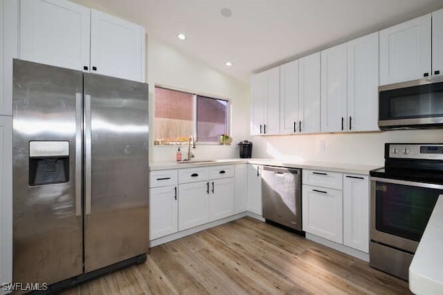 kitchen featuring lofted ceiling, sink, stainless steel appliances, and white cabinetry