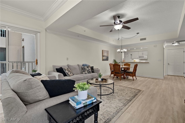 living room with a raised ceiling, light wood-type flooring, crown molding, a textured ceiling, and ceiling fan with notable chandelier