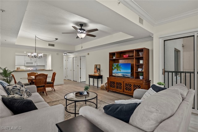 living room with ornamental molding, light wood-type flooring, a raised ceiling, and ceiling fan with notable chandelier