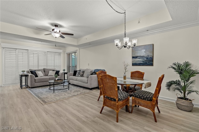 dining space featuring ceiling fan with notable chandelier, a raised ceiling, ornamental molding, and light hardwood / wood-style floors