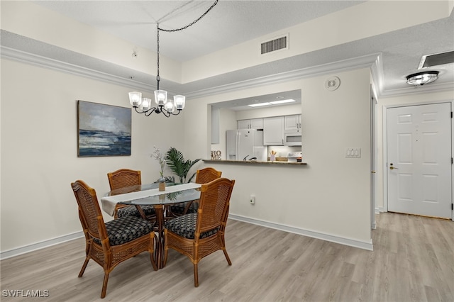 dining room with ornamental molding, light wood-type flooring, a raised ceiling, and a chandelier