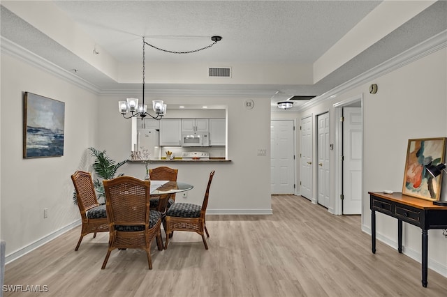 dining area featuring a textured ceiling, an inviting chandelier, light hardwood / wood-style floors, a tray ceiling, and crown molding