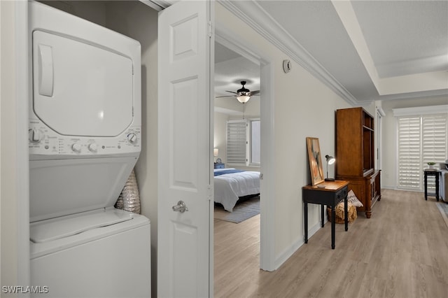 laundry room with ceiling fan, light wood-type flooring, and stacked washer / dryer