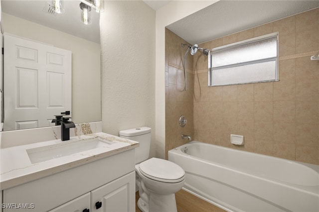 full bathroom with hardwood / wood-style floors, tiled shower / bath combo, vanity, and toilet