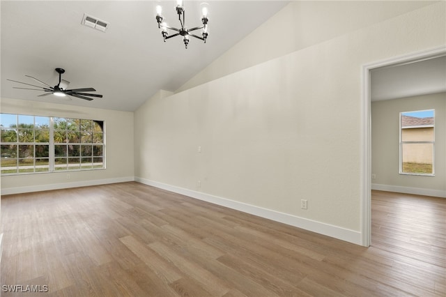 empty room featuring a healthy amount of sunlight, vaulted ceiling, ceiling fan with notable chandelier, and light hardwood / wood-style flooring