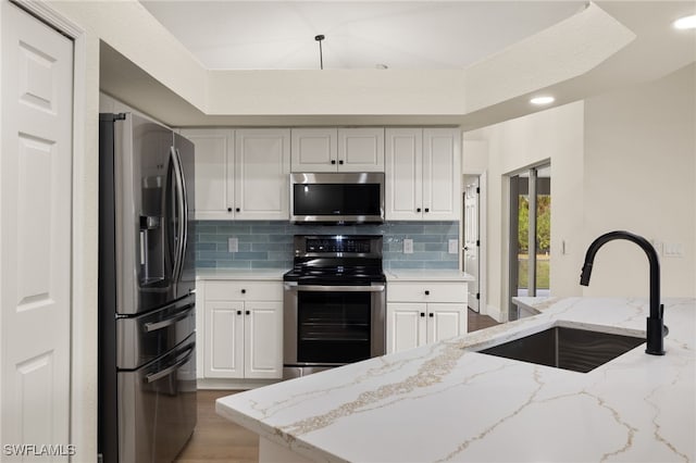 kitchen featuring decorative backsplash, sink, white cabinetry, light stone countertops, and appliances with stainless steel finishes