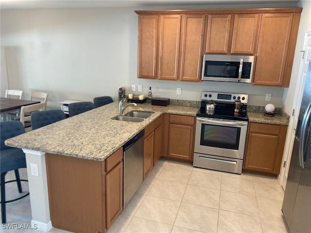 kitchen with sink, light stone countertops, appliances with stainless steel finishes, light tile patterned flooring, and kitchen peninsula