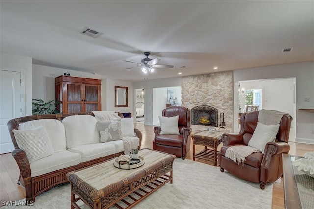 living room with ceiling fan, light hardwood / wood-style flooring, and a stone fireplace