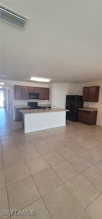 kitchen with black appliances, sink, light tile patterned floors, an island with sink, and dark brown cabinetry