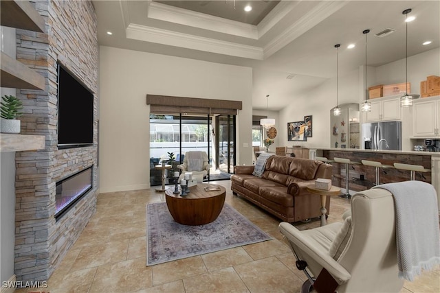 living room featuring a towering ceiling, light tile patterned flooring, a tray ceiling, crown molding, and a stone fireplace