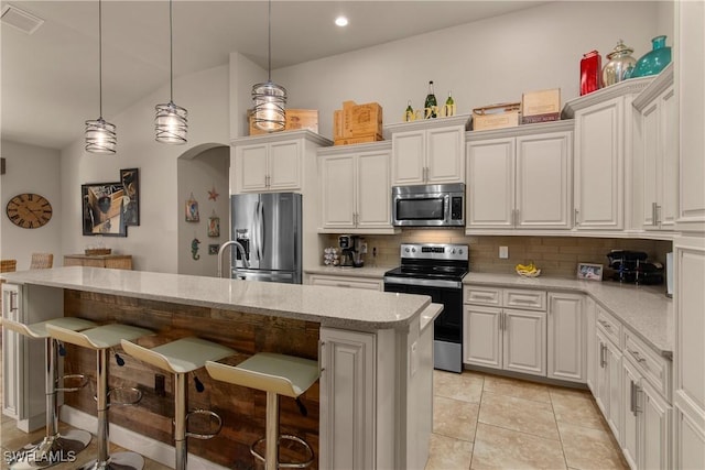 kitchen with a breakfast bar, stainless steel appliances, an island with sink, and decorative backsplash